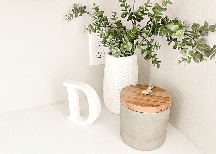 a plant, a wooden letter D and a decorative jar sitting on top of a white counter