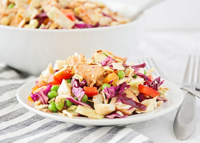 a plate of crunchy Asian chicken salad filled with vegetables on a white plate with a white bowl full in the background