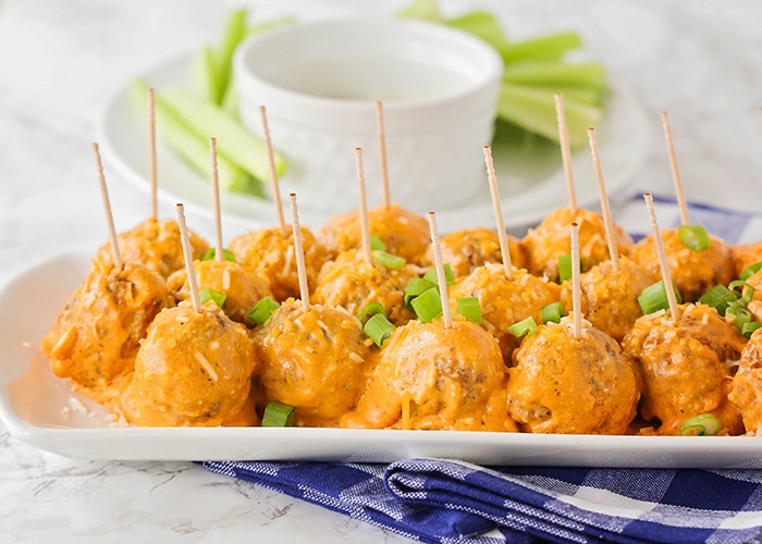 a tray of these easy buffalo chicken meatballs topped with green onions and toothpicks inside each one. A plate of celery is in the background.