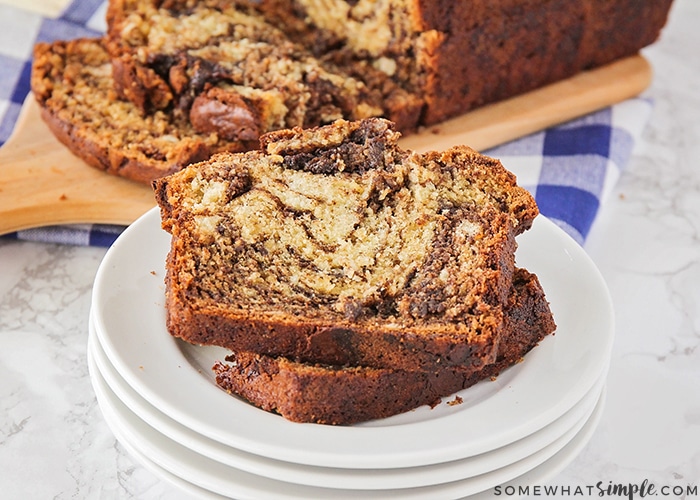 a stack of white plates with two slices of chocolate banana bread on top with a loaf in the background