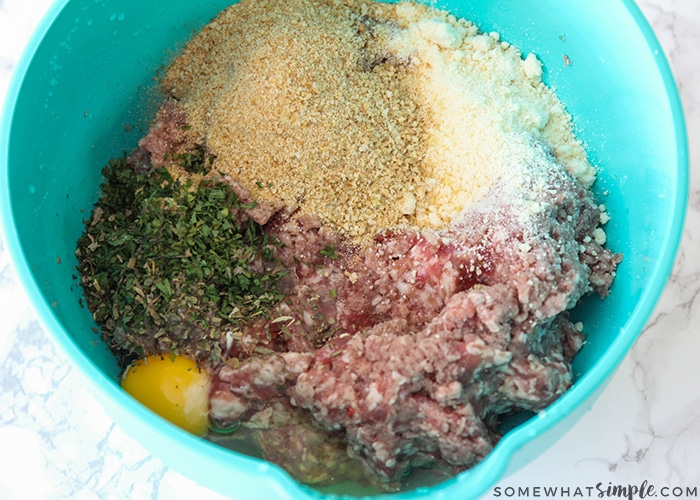 all of the ingredients to make homemade meatballs in a blue mixing bowl