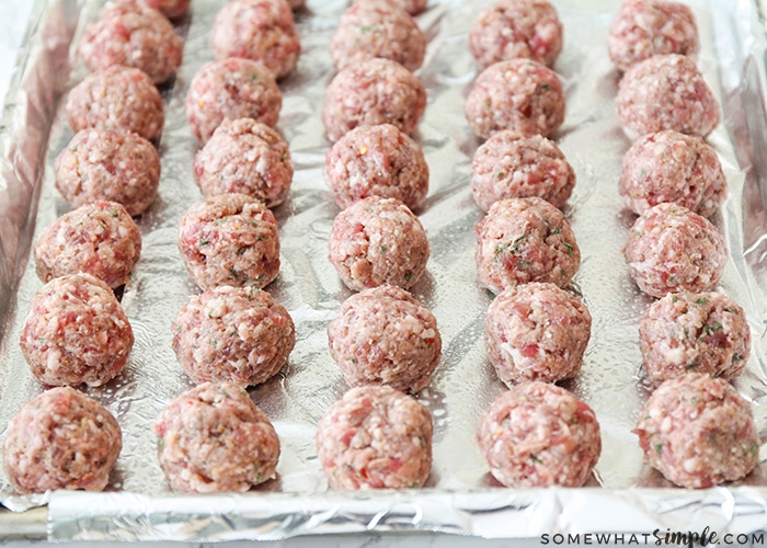 a tray of raw homemade meatballs on a baking sheet lined with foil.