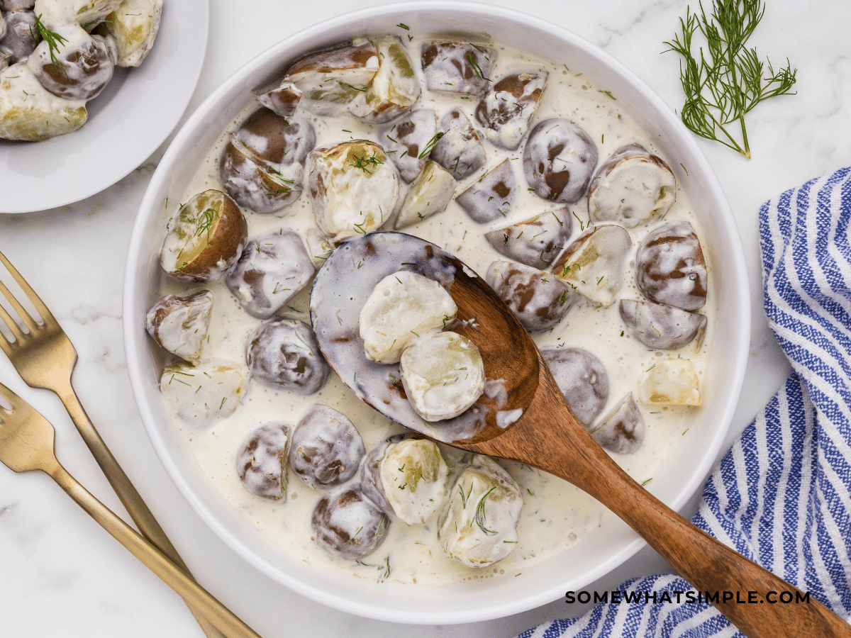 Creamy Dill Potatoes in a white serving bowl with wooden spoon