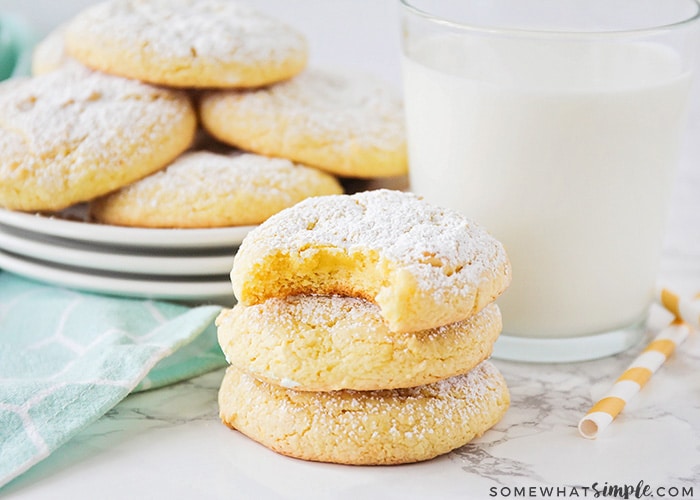 a stack of lemon cake mix cookies with a glass of milk and a plate of more cookies in the background