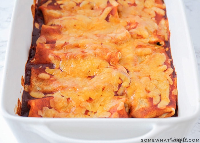 a tray of enchilada style burritos that have been baked in the oven and are topped with melted cheddar cheese