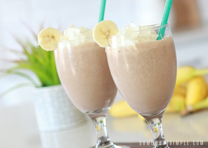two glasses filled with this Dirty Monkey recipe topped with a banana and whipped cream