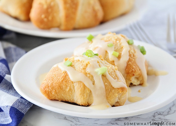 a plate with two chicken crescent roll ups topped with green onions and cream of chicken soup drizzled on top. Behind the plate is another plate filled with these chicken crescent rolls.