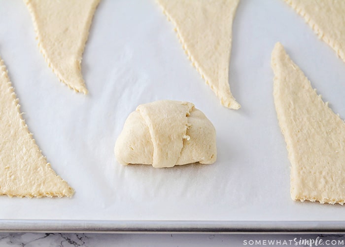 triangles of crescent roll dough on a baking sheet. The one in the middle has been completely folded over to form a roll up.