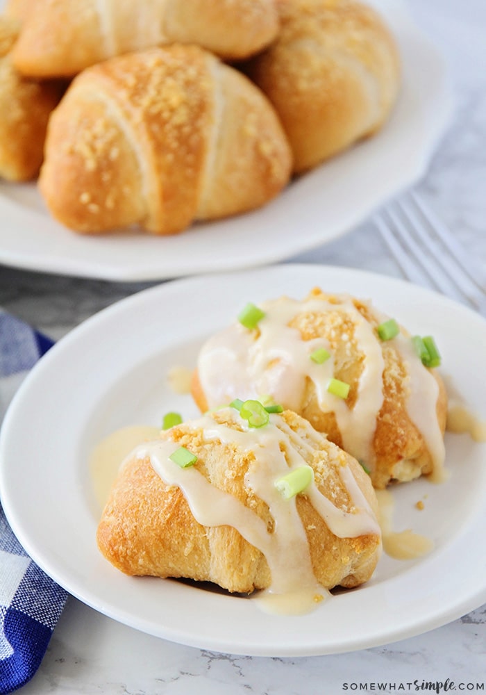 looking down on a plate of two crescent chicken rolls topped with green onions and cream of chicken soup drizzled on top. There's another plate topped with golden brown crescent roll ups.