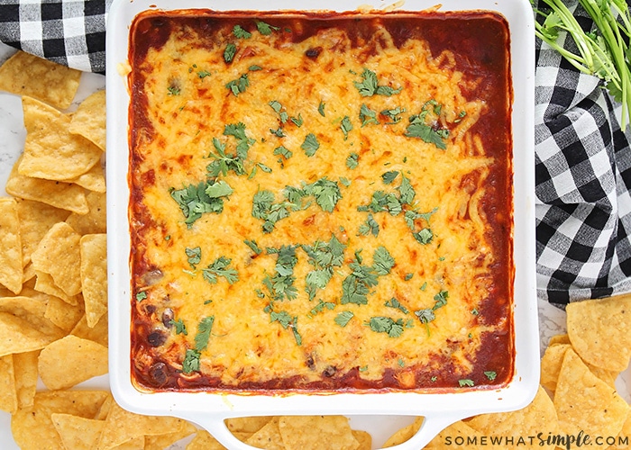 looking down on a baking pan filled with this easy enchilada dip recipe with tortilla chips on the counter next to it