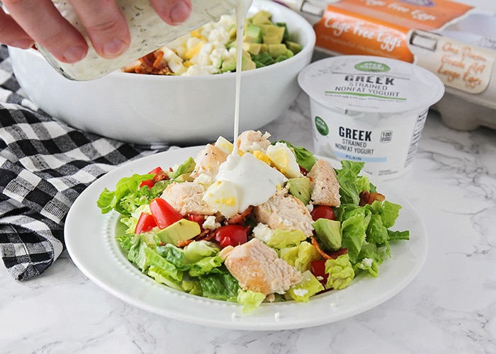 homemade buttermilk ranch dressing being poured over the top of a cobb salad