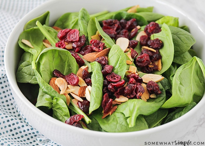 a close up of a bowl filled with baby green spinach, cranberries and sliced almonds