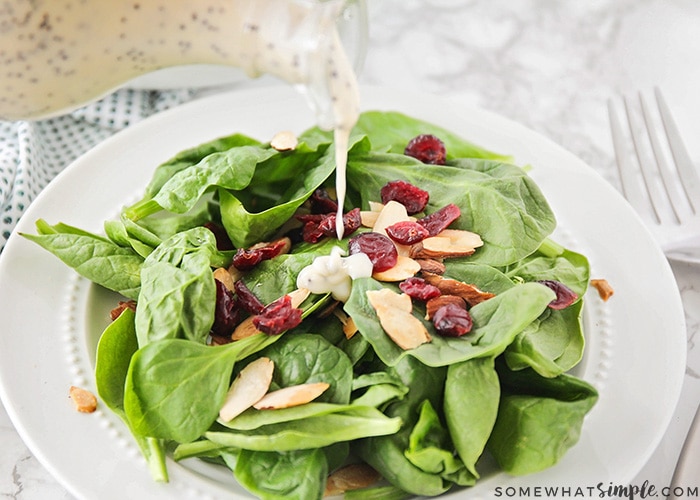 poppy seed dressing being poured over the top of a salad