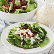 a plate filled with a spinach salad with cranberries and topped with almonds and a homemade poppy seed dressing.