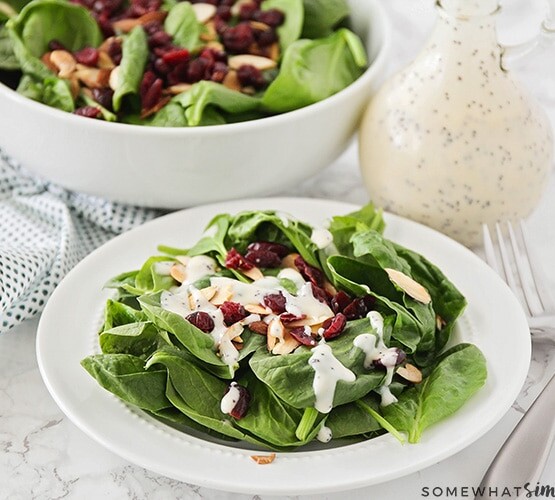 a plate filled with a spinach salad with cranberries and topped with almonds and a homemade poppy seed dressing.