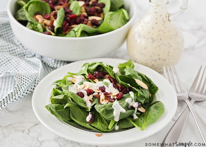 a plate filled with a spinach salad with cranberries and topped with almonds and a homemade poppy seed dressing.