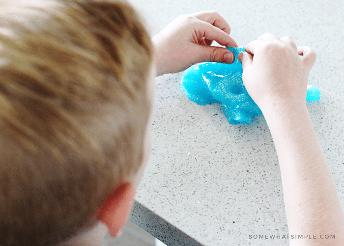 A child showing how to make blue slime at home while sitting at the kitchen counter.