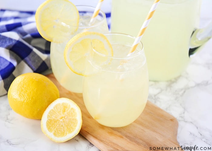 two glasses and a pitcher filled with homemade lemonade with a couple of lemons laying on the counter