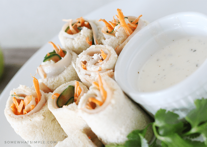 looking down on several sushi sandwich rolls filled with turkey, carrots and cucumbers on a plate next to a small side dish of ranch dressing