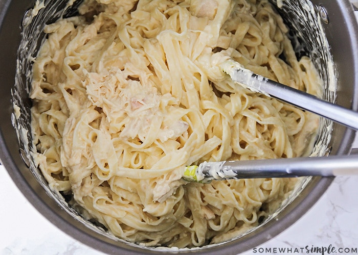 a pot of chicken tetrazzini with alfredo sauce in a black pot being mixed together