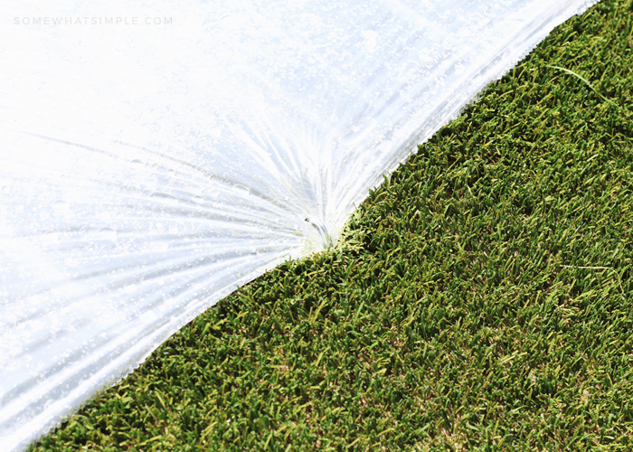 a close up of a stake put through the side of a plastic drop cloth to make a homemade slip and slide