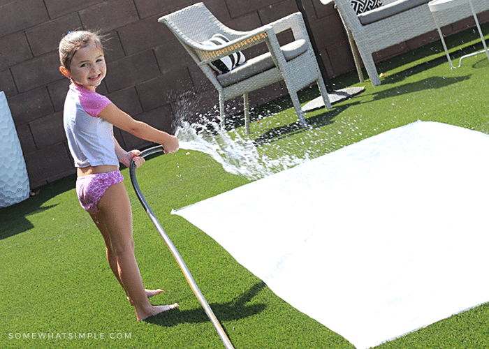 a little girl spraying a homemade slip and slide with water from a hose