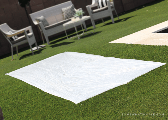 a plastic drop cloth on grass that will be used as a DIY slip and slide