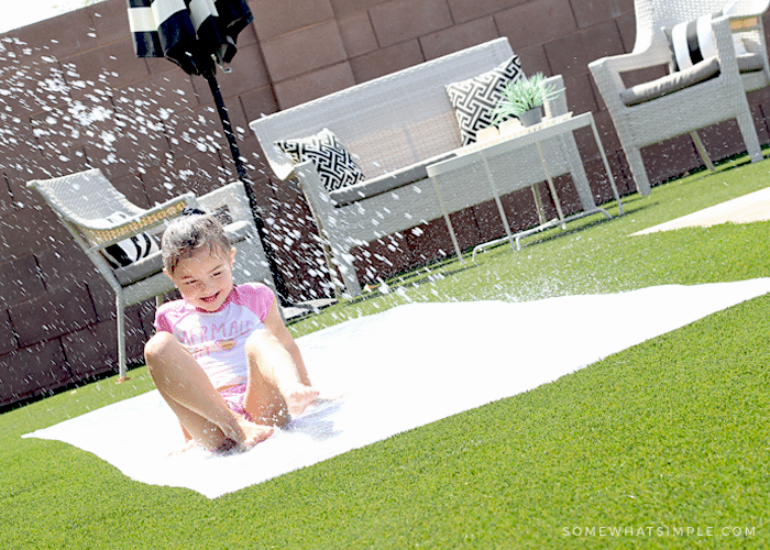 a little girl sliding through spraying water on a diy slip and slide in her backyard