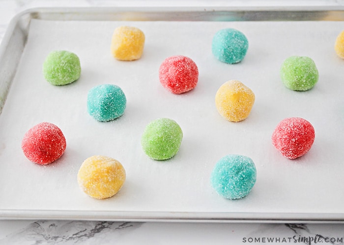 a baking sheet with raw red, green, blue and yellow cookie dough covered with sugar on a baking sheet before they go in the oven