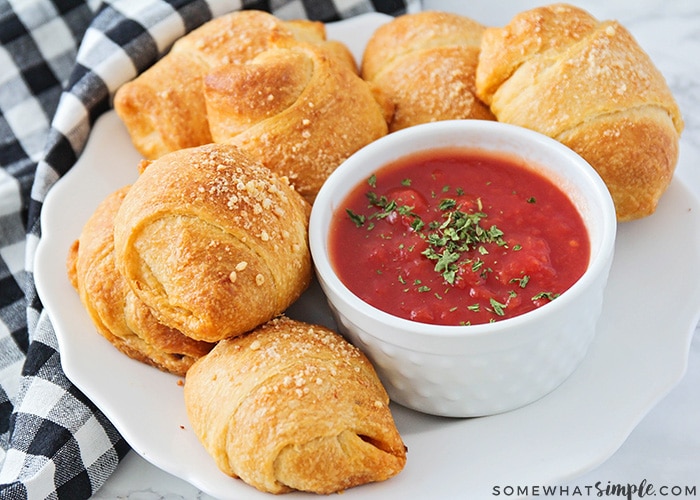 a plate of pizza bites on a white plate with a checkered napkin next to it with a side of marinara dipping sauce