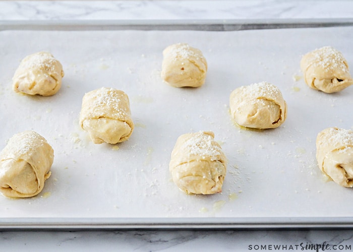 homemade pizza bites on a baking sheet rolled up and ready to be placed in the oven