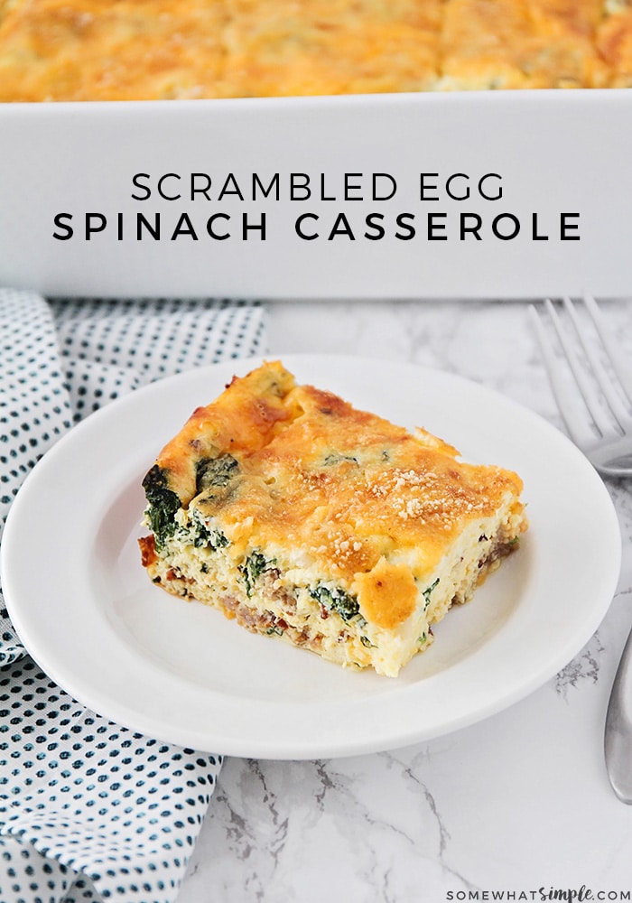 a square of breakfast casserole on a white plate. Piece of spinach and sausage can be seen from the side. Behind the plate on the counter is a white casserole dish filled with this easy egg casserole recipe. The words scrambled egg spinach casserole is written near the top of the image.