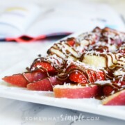 a plate of apple nachos topped with slices of strawberries and bananas, shredded coconut and chocolate drizzled over the top