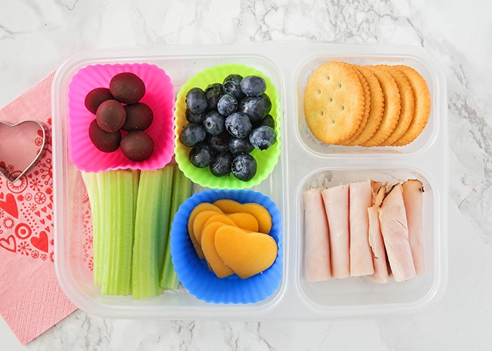 a bento box lunch with fruit, turkey, cheese and celery