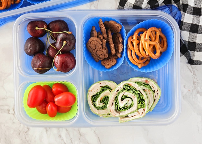 a bento box with tomatoes, cherries, a sandwich and snacks