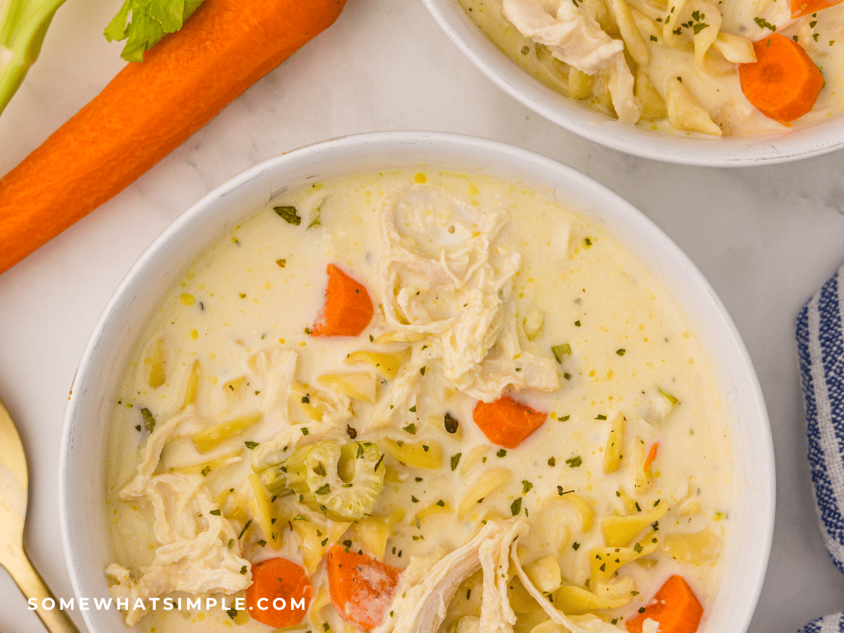 2 bowls of Crockpot Creamy Chicken Noodle Soup next to a long carrot
