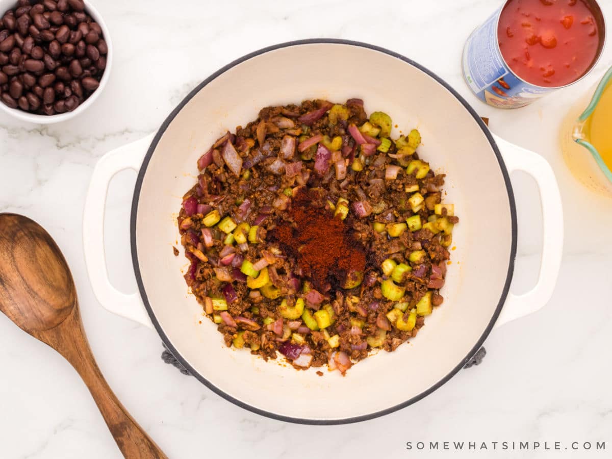 adding paprika to a pot of chorizo and vegetables