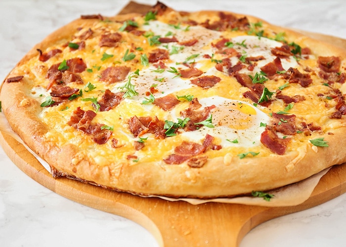A breakfast pizza topped with eggs, bacon and cheese on a pizza tray 