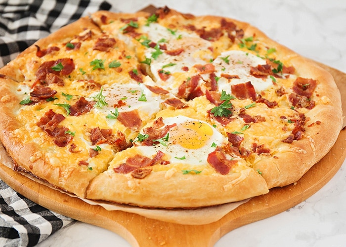 a cooked breakfast pizza topped with cheese, eggs and bacon