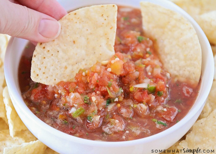 a hand dipping a tortilla chip into a white bowl of this blender salsa.