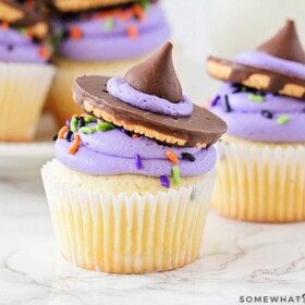 two Witch Hat Cupcakes on a counter with a tray filled behind them