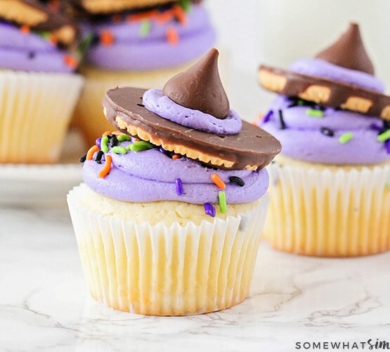 two Witch Hat Cupcakes on a counter with a tray filled behind them