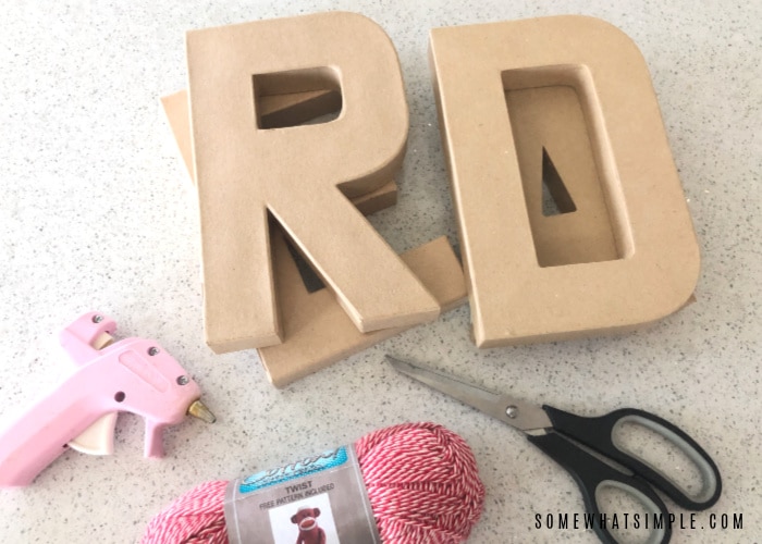 wood letters, yarn, scissors and a glue gun laying on a white counter