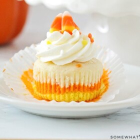 a Candy Corn Cupcake with orange, yellow and white layers on a plate topped with cream cheese frosting