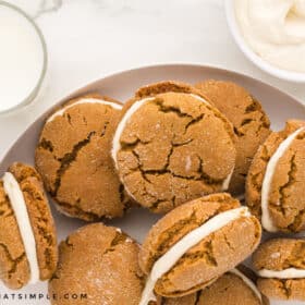 ginger sandwich cookies on a white plate next to a glass of milk