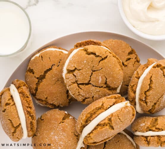 ginger sandwich cookies on a white plate next to a glass of milk