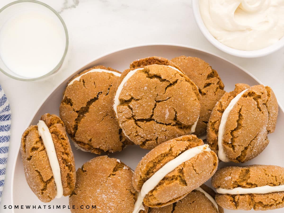 ginger sandwich cookies on a white plate next to a glass of milk