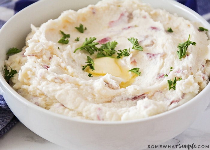 A white bowl of cream cheese mashed potatoes topped with a melting pad of butter and parsley