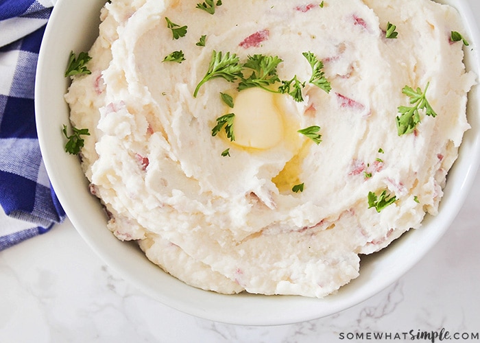 looking down on a bowl of mashed potatoes made with cream cheese with a yellow pad of butter half melted in the center and parsley sprinkled over the top