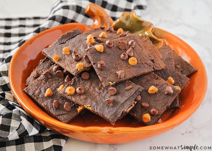 an orange pumpkin shaped bowl filled Pumpkin Spice Brownie Brittle sitting on a counter and a black and white checkered cloth napkin.